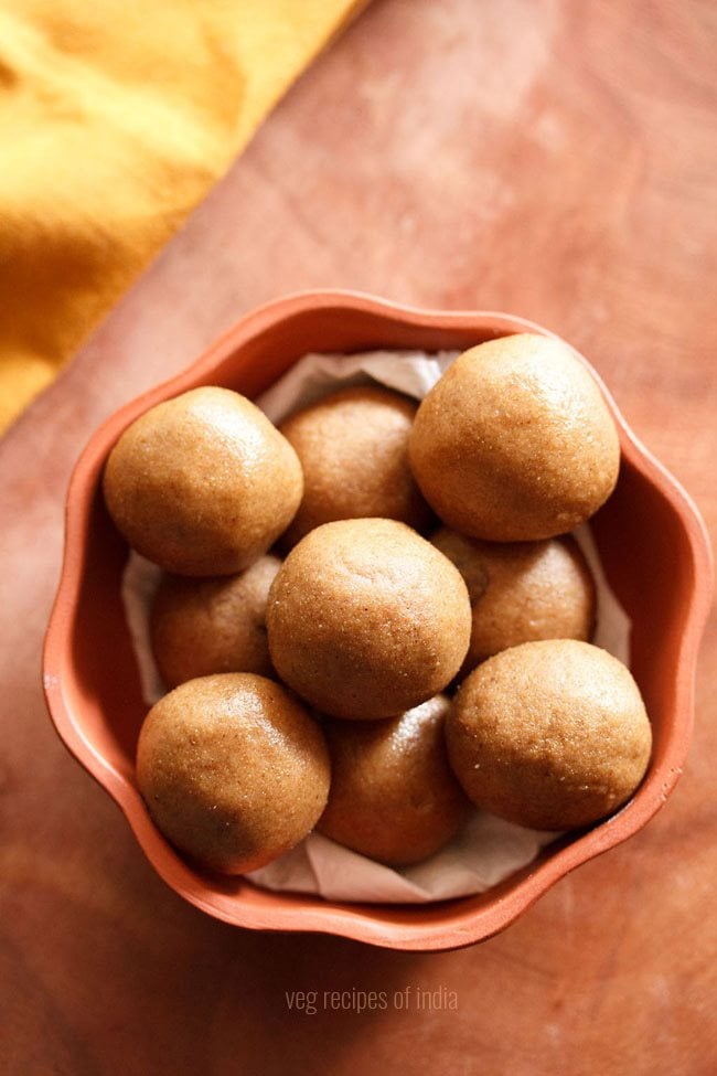 atta ladoo served in a brown bowl with text layover. 