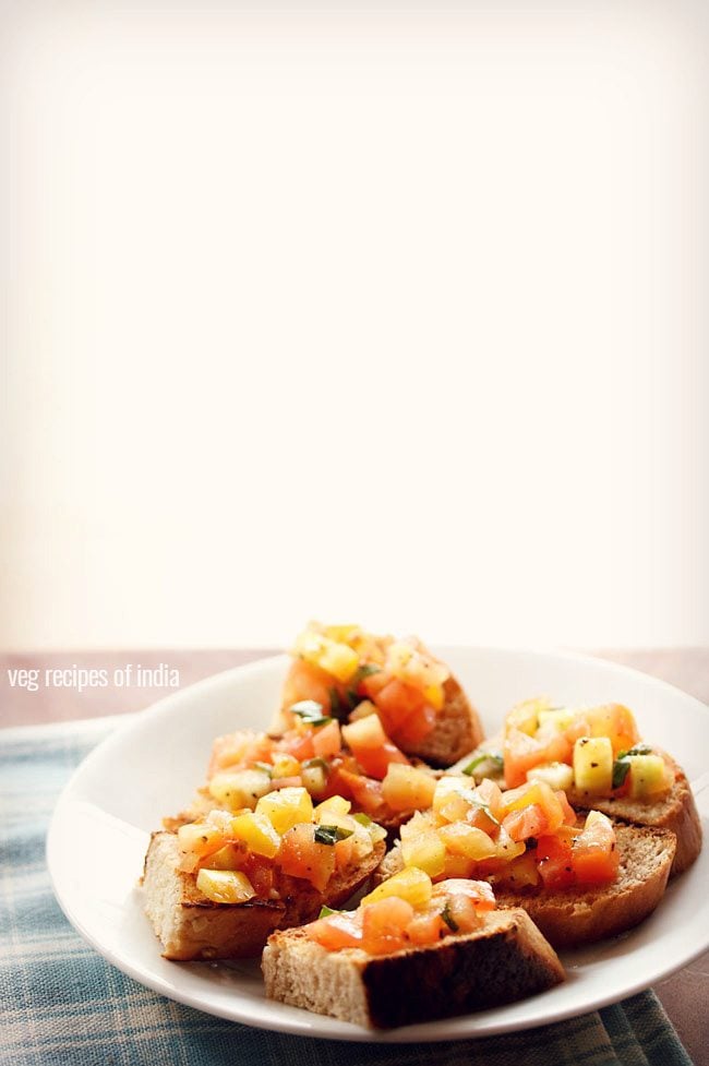 hero shot of tomato bruschetta recipe: white plate with 6 pieces of tomato bruschetta on a blue and white gingham napkin. 