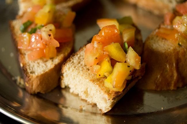 silver platter with toasted bread topped with tomato bruschetta topping. 