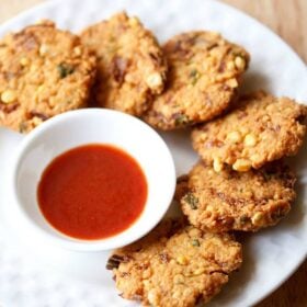 dal vada arranged neatly on a white plate next to a small white bowl of red chutney