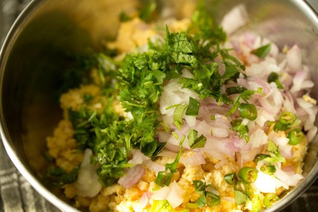 onions, spices and herbs added to the chana dal mixture in a steel mixing bowl