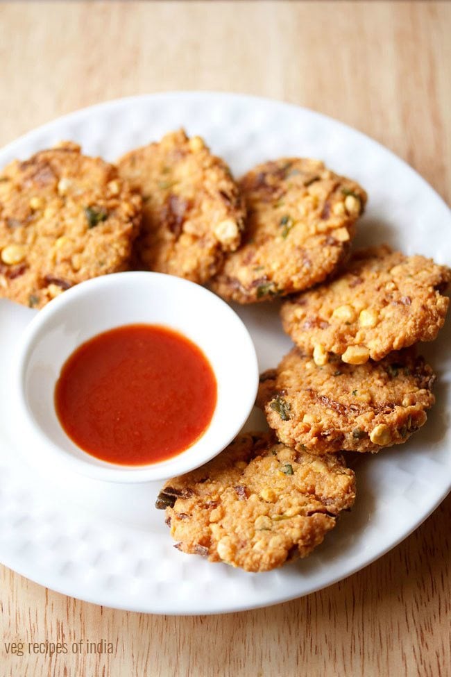 dal vada arranged neatly on a white plate next to a small white bowl of red chutney