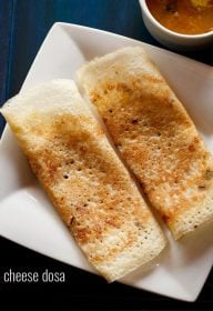 folded cheese dosa served on a square white plate with a bowl of sambar kept in the top right side and text layover.