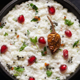 curd rice garnished with chopped coriander leaves, fresh pomegranate arils and fried sun dried chili and served in a wooden bowl.