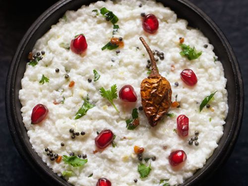 curd rice garnished with chopped coriander leaves, fresh pomegranate arils and fried sun dried chili and served in a wooden bowl.