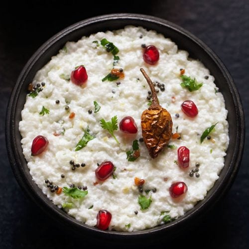 curd rice garnished with chopped coriander leaves, fresh pomegranate arils and fried sun dried chili and served in a wooden bowl.