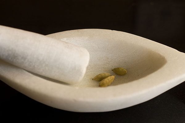 crushing green cardamom in a mortar pestle