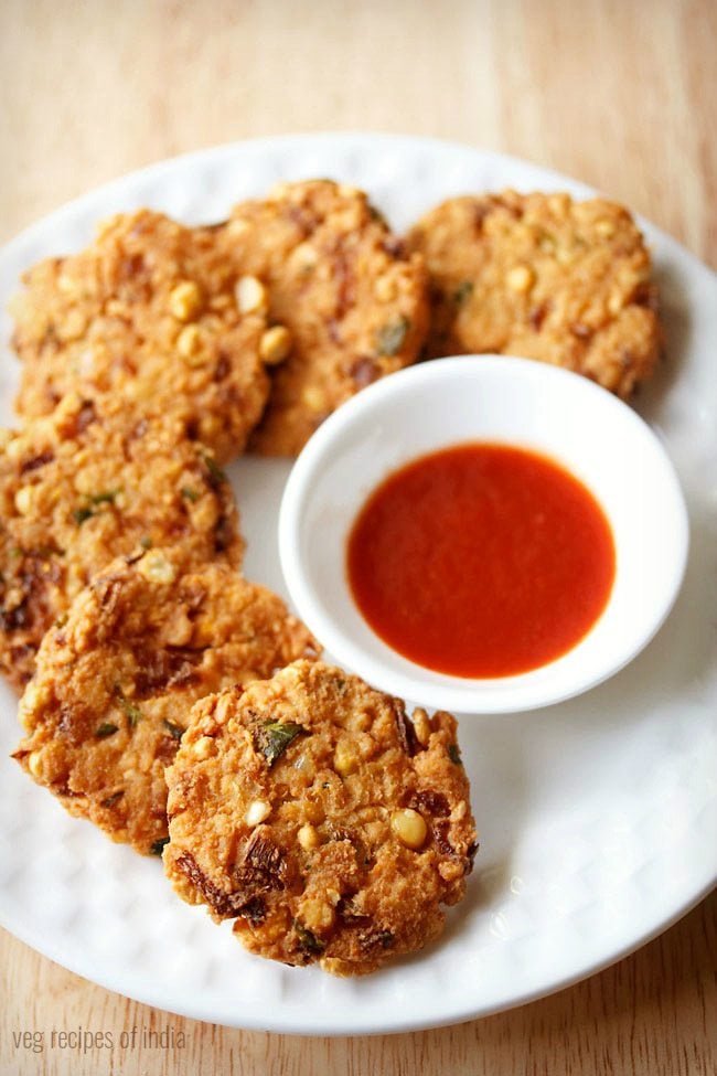 dal vada arranged neatly on a white plate next to a small white bowl of red chutney