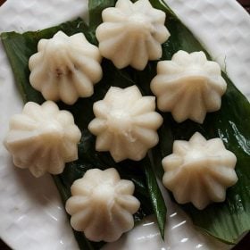 top shot of dry fruit modak placed on a turmeric leaf and served on a white plate.