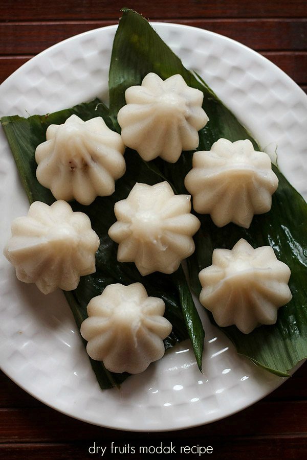 top shot of dry fruit modak placed on a turmeric leaf and served on a white plate.