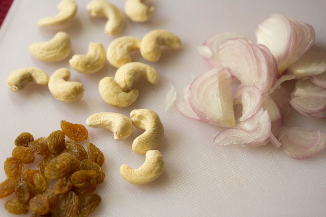 cashews, raisins, sliced onions on a white chopping board