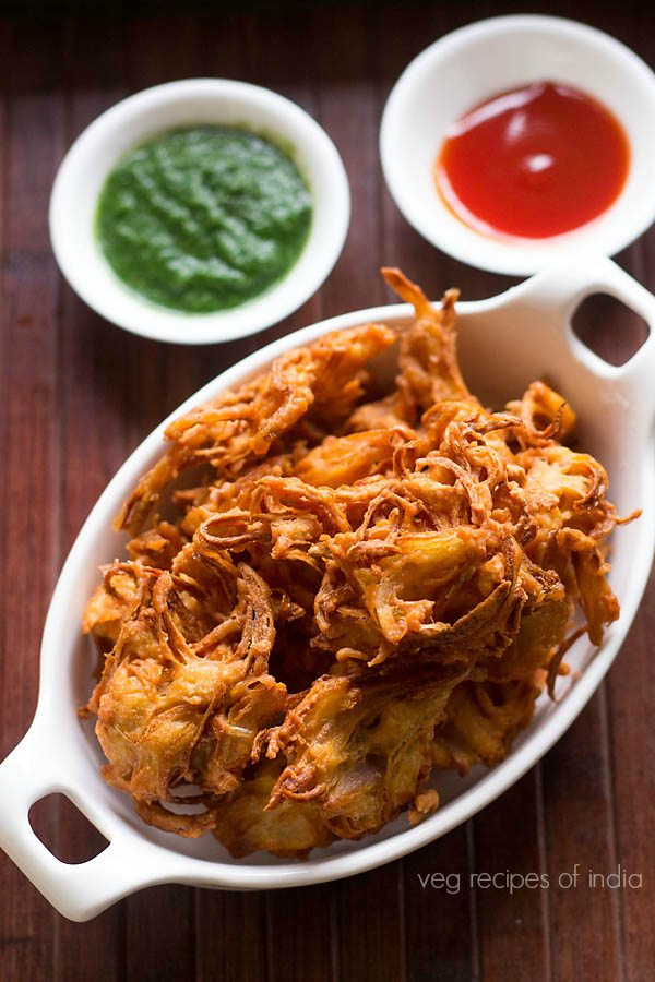 kanda bhaji served in white tray with a side of green chutney and tomato sauce