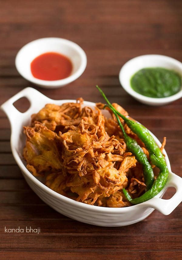 kanda bhaji served in white tray with a side of fried green chilies, green chutney and tomato sauce