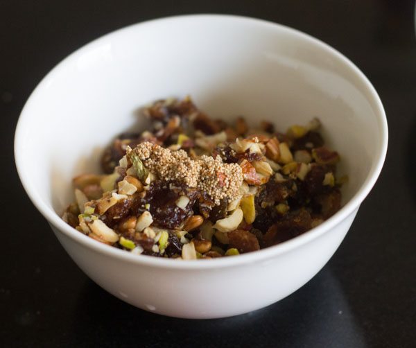 sautéed poppy seeds added to the roasted dry fruit mixture in a white bowl. 