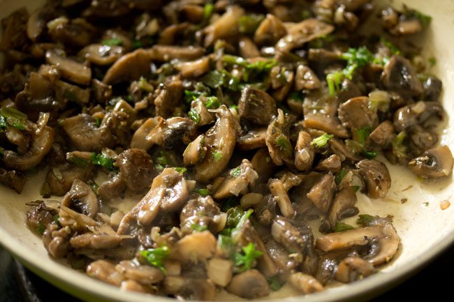 mixing the herbs with the mushrooms in the pan to make mushroom stuffing for mushroom sandwich