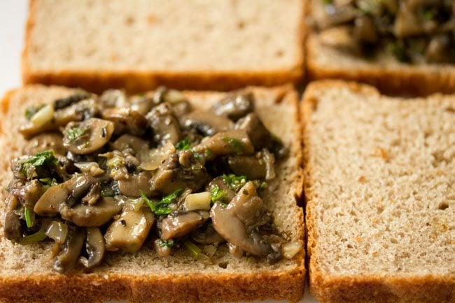 spreading a portion of the cooked mushroom filling on the bread slices. 