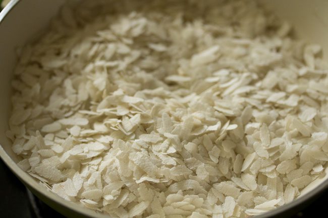 thick poha added to hot pan for making poha laddu. 