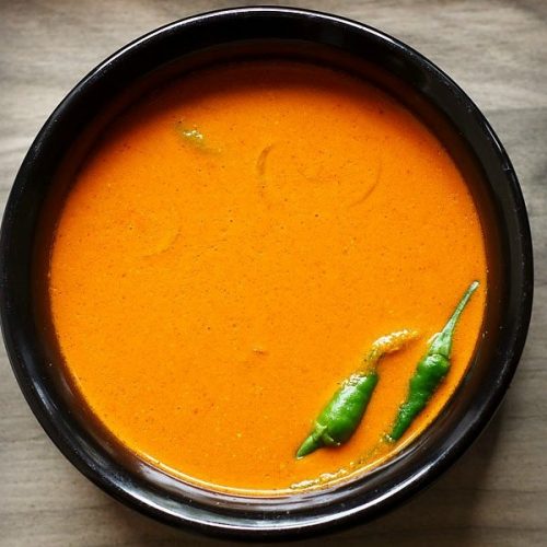 sorak curry or goan coconut curry in a black bowl with green chillies at side.