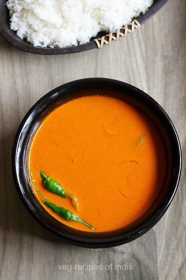 sorak curry in black bowl with green chilies at side with a tray of steamed rice above.