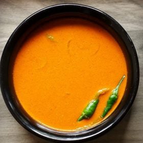 sorak curry in a black bowl with green chillies at side.