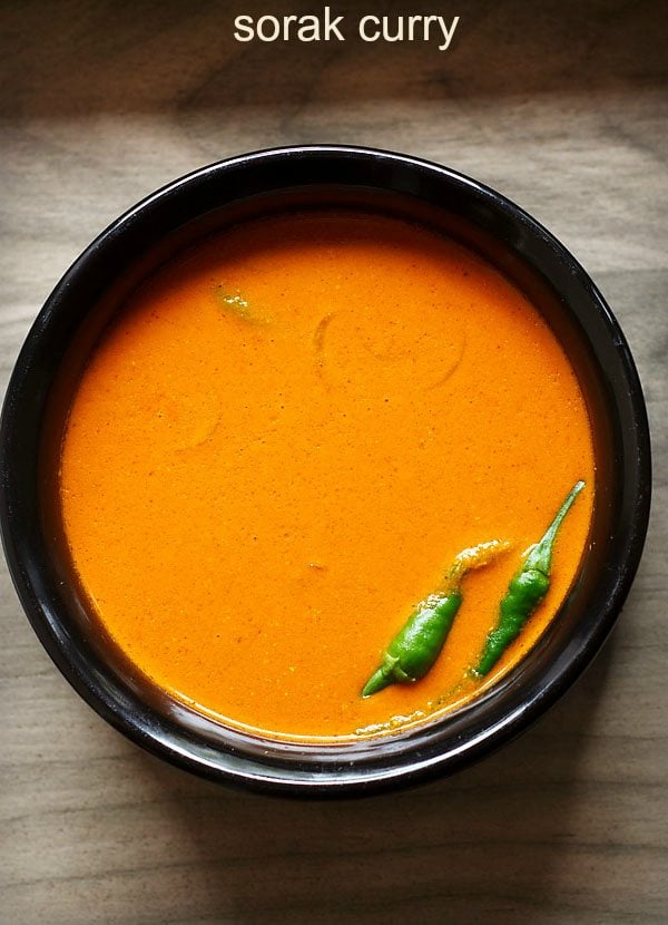 sorak curry in a black bowl with green chillies at side.