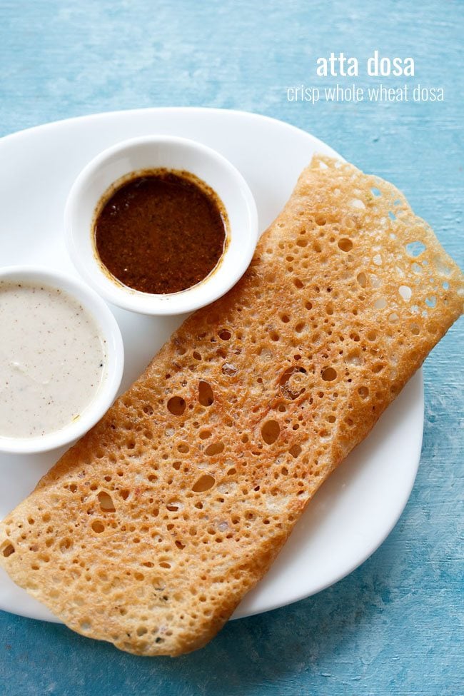 wheat dosa served on a white plate with chutneys in 2 small bowls