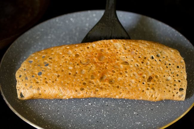 lifting cooked wheat dosa with a spatula