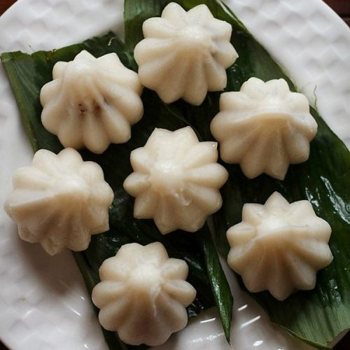 top shot of dry fruit modak placed on a turmeric leaf and served on a white plate.