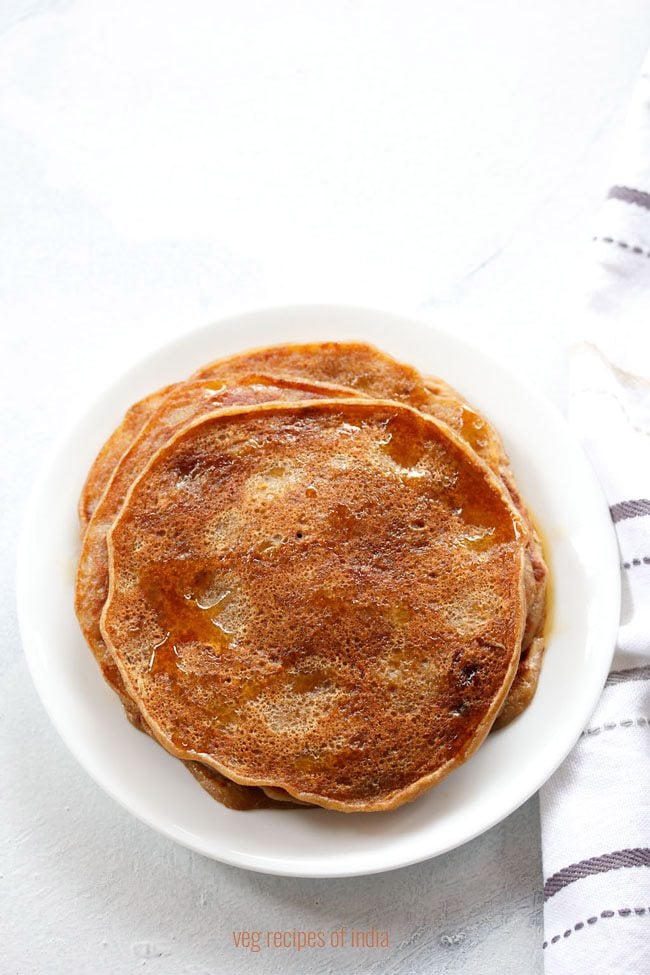 eggless banana pancakes drizzled with maple syrup on a white plate on a white board