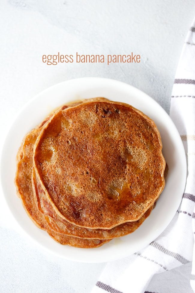 eggless banana pancakes drizzled with maple syrup on a white plate on a white board