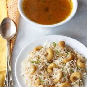 kaju pulao served on a white plate with spoon and shorba bowl on the side.