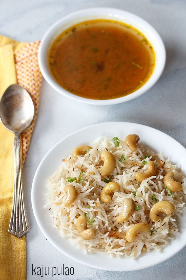 kaju pulao served on a white plate with spoon and shorba bowl on the side.