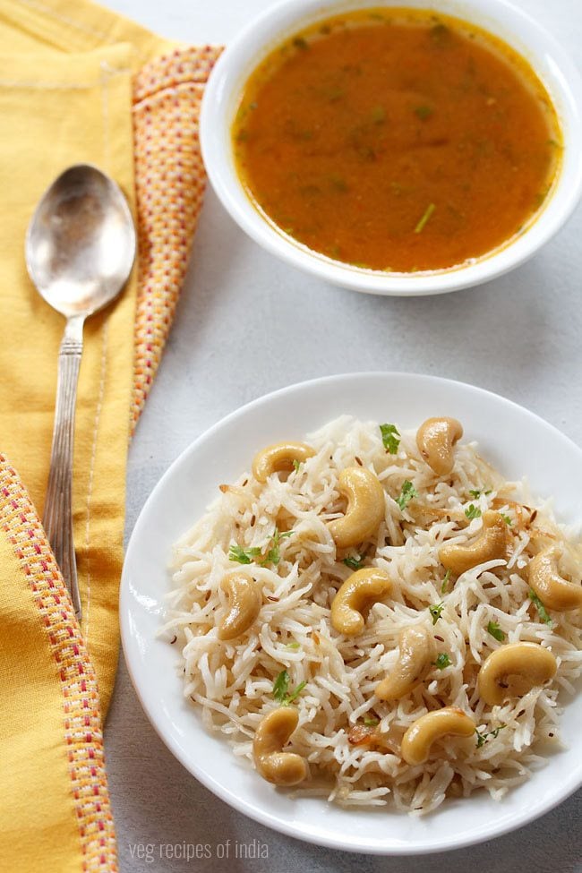 kaju pulao served on a white plate with a spoon and shorba bowl on the side.
