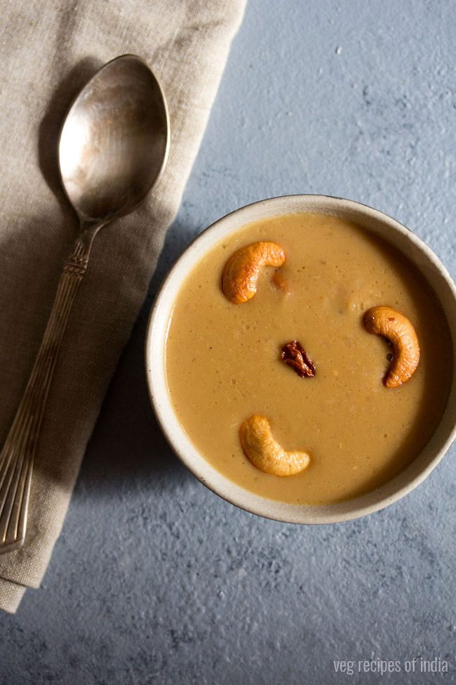 Top shot of pasi paruppu payasam, garnished with fried cashews, served in a bowl with spoon on left side and text halfway through. 