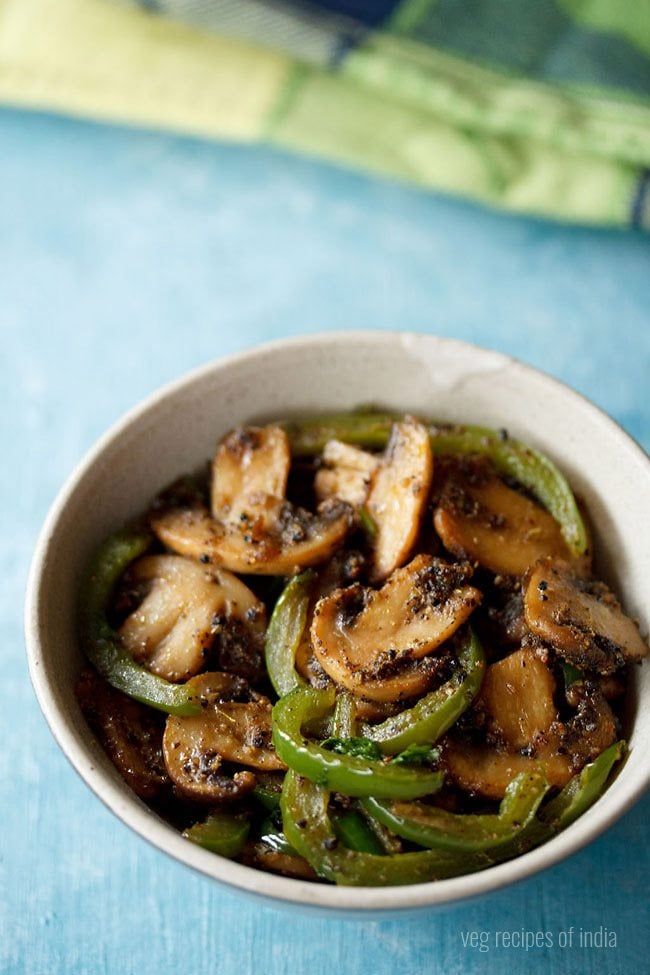 mushroom pepper fry served in a cream colored ceramic bowl with text layover. 