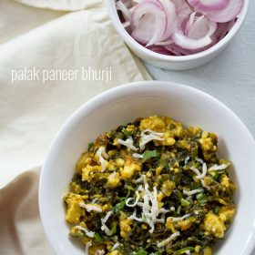 palak paneer bhurji garnished with grated paneer and served in a white bowl along with a side of a bowl of onions.