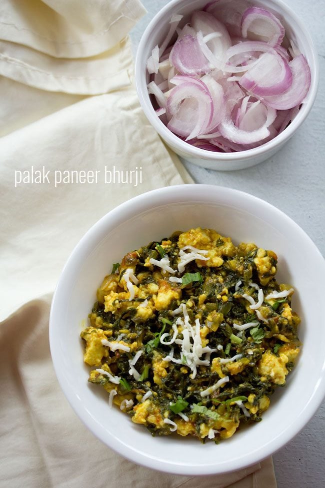 palak paneer bhurji garnished with grated paneer and served in a white bowl along with a side of a bowl of onions.