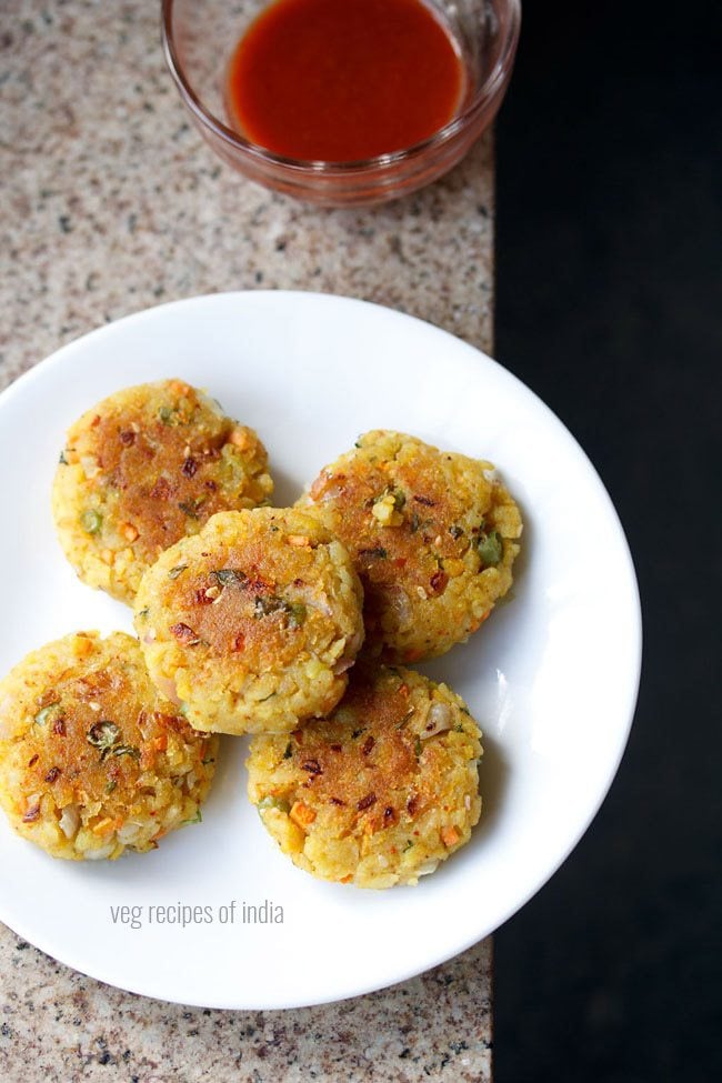 poha cutlet served on a white plate with a bowl of tomato ketchup kept on the top and text layover.