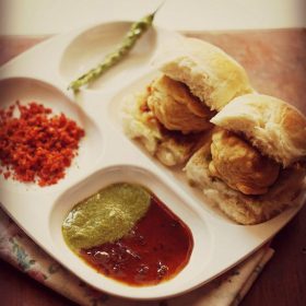 vada pav served in a white plate with chutneys and fried green chili.