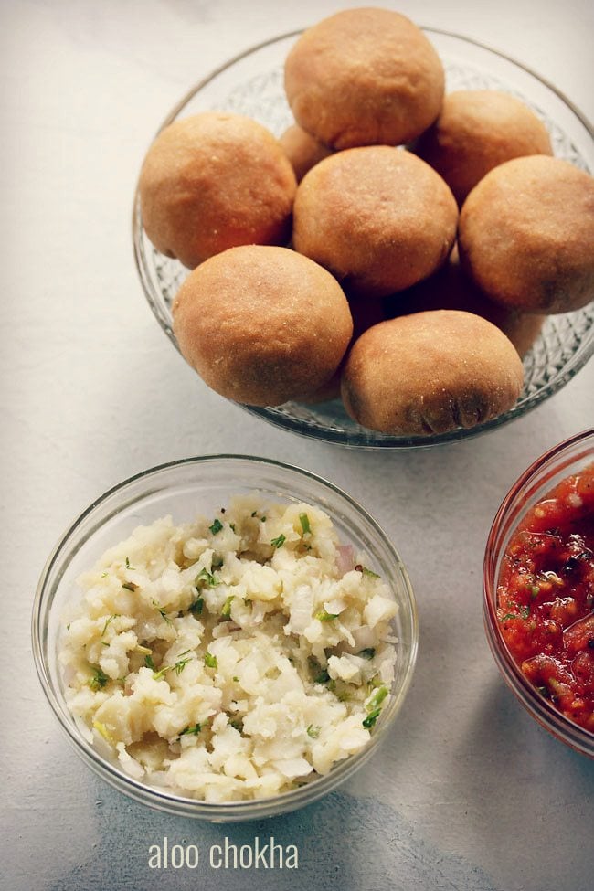 aloo chokha served in a glass bowl with littis in a large bowl and text layover.