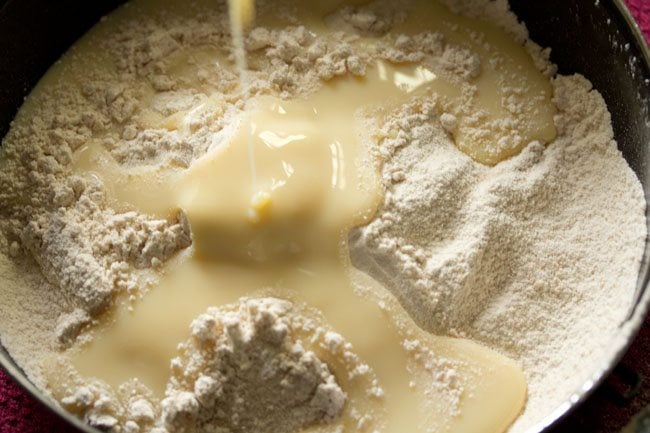 sweetened condensed milk being poured on the sifted wheat flour