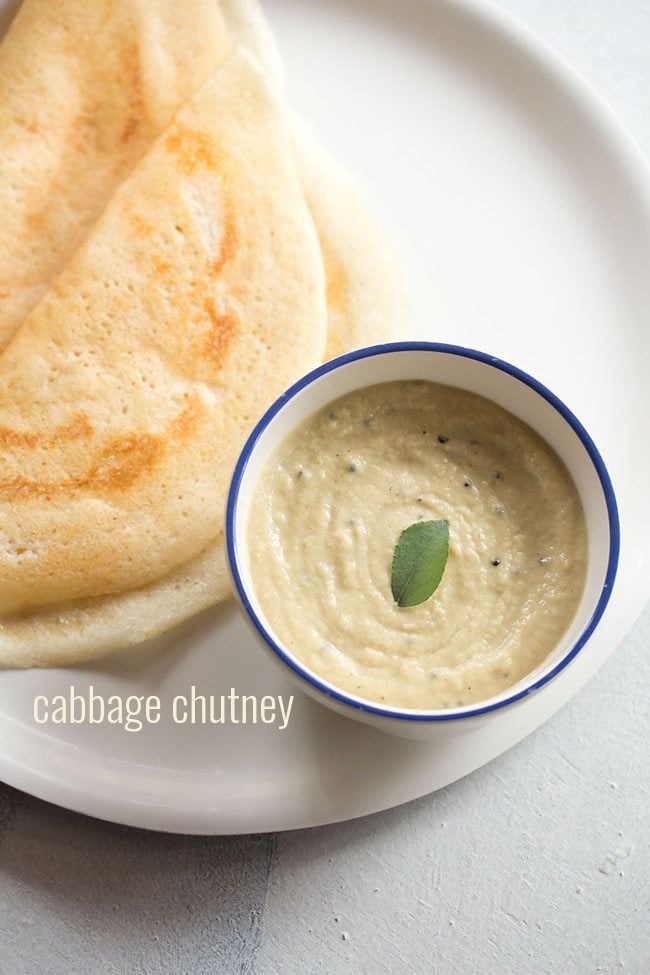 cabbage chutney with a curry leaf in center in a blue rimmed white bowl with two dosa by the side in a white plate