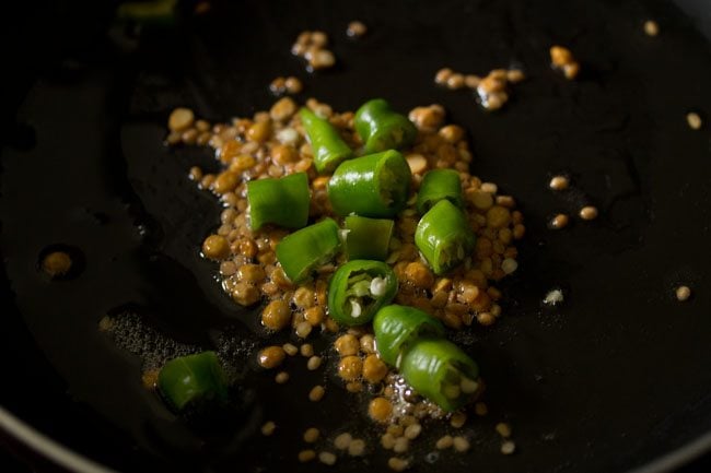 chopped green chillies on top fried golden lentils in black pan