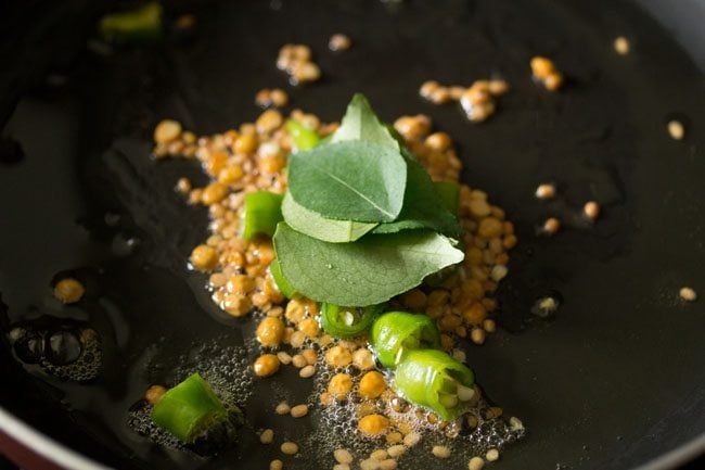 curry leaves  on top of green chillies in black pan