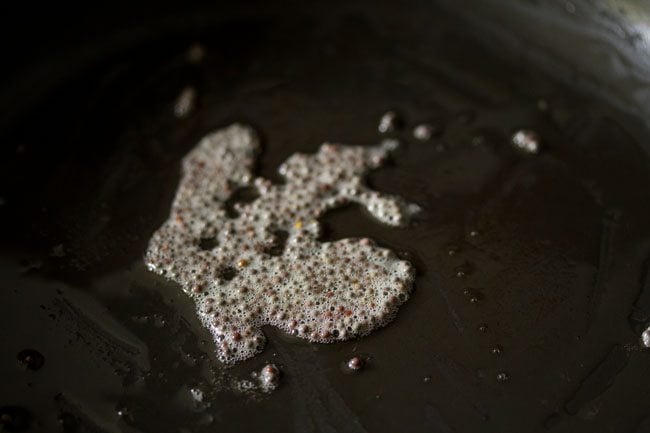 mustard seeds frying in oil in black pan