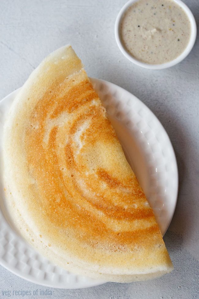 ghee roast dosa folded and served on a white plate with a small bowl of coconut chutney kept on the top right side. 