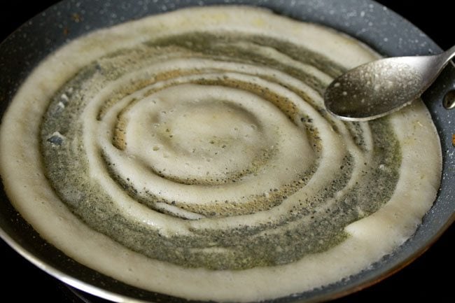 spreading ghee on the dosa with a spoon. 