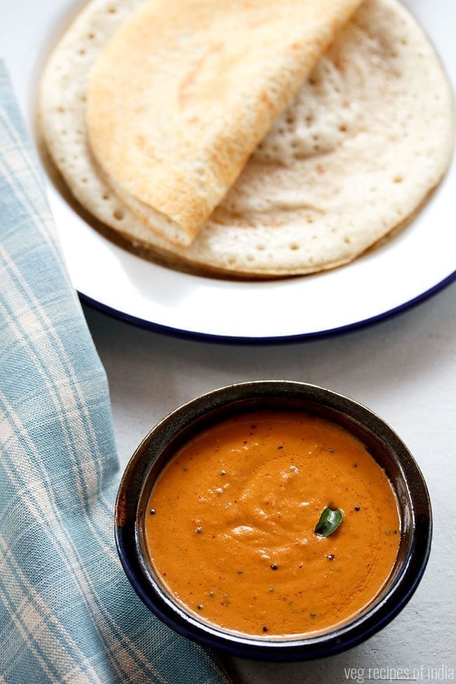 kara chutney served in a black bowl with a plate of dosas kept in the background and text layover. 