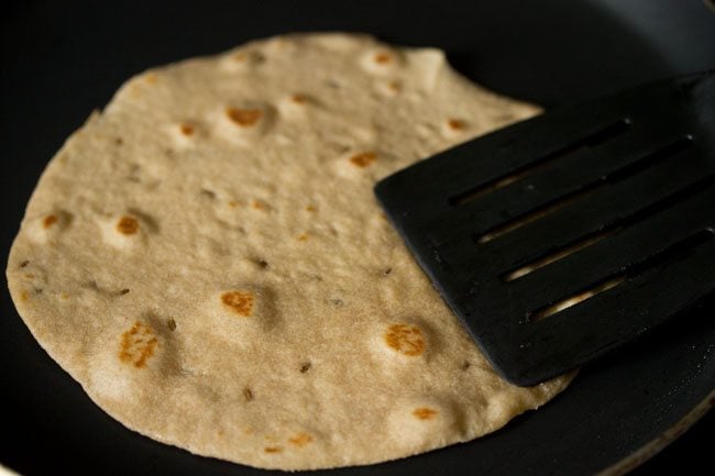 pressing the edges of the roti to roast it evenly and crisp. 