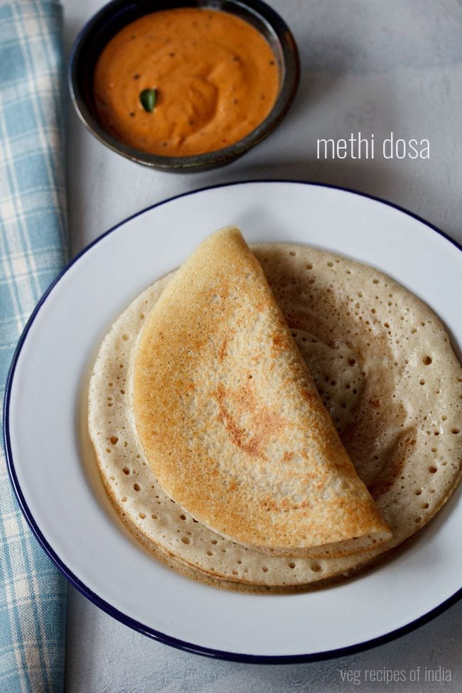 methi dosa served on a blue rimmed white plate with a bowl of kara chutney kept on the top side and text layover. 